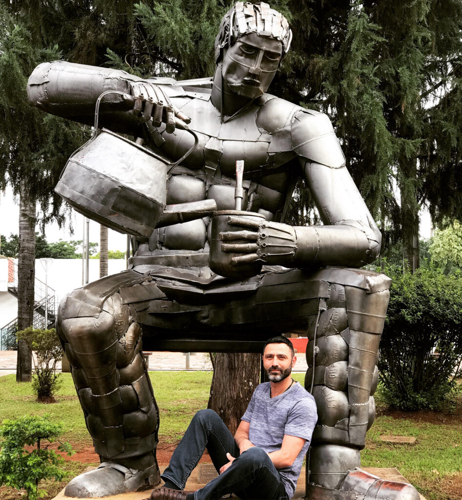 Traditional wooden Yerba Mate calabash gourd with a stainless steel bombilla straw, sitting next to a rustic El Matero statue, Posadas 2019